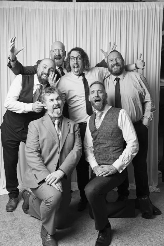 Seven friends in suits pull faces and throw up peace signs